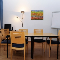 Kleiner Raum mit Tisch, Stühlen, Büchern und einer Flipchart