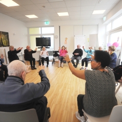 Eine Gruppe von Seniorinnen und Senioren sitzt im Kreis und macht gymnastische Übungende